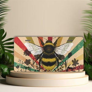 May include: A retro-style license plate featuring a yellow and black bumblebee with wings spread, surrounded by a colorful rainbow pattern and green foliage.