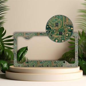 May include: A green and gold license plate frame with a circuit board pattern. The frame is made of metal and has a smooth finish.