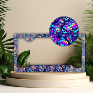May include: A black license plate frame with a colorful skull pattern. The frame is made of metal and has a glossy finish. The skulls are in shades of blue, purple, pink, and yellow.