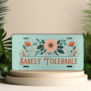 May include: A light blue license plate with a floral design in shades of green, black, and orange. The text "Barely Tolerable" is printed in orange on the plate.