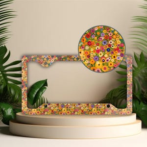 May include: A colorful floral license plate frame with a bright yellow, orange, red, pink, purple, and blue flower pattern. The frame is made of metal and has a shiny finish.