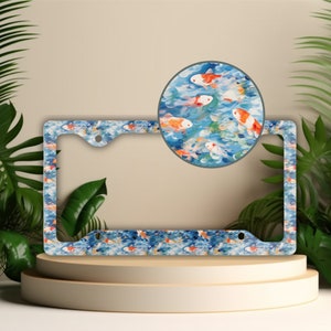 May include: A blue and white license plate frame with a pattern of orange and white koi fish swimming in water. The frame has a silver metal finish and is designed to fit a standard US license plate.