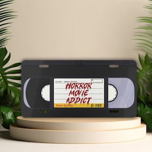 May include: A black VHS tape with a label that reads "HORROR MOVIE ADDICT" in red dripping letters. The label also says "Extra Quality" and "E-180".