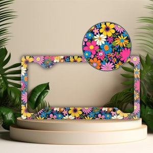 May include: A colorful floral license plate frame with a dark blue background. The frame is decorated with pink, yellow, orange, and blue flowers. The frame is shown on a light brown surface.