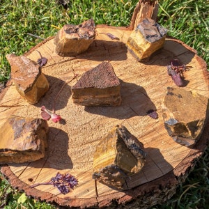 May include: Six tiger's eye stones of various sizes and shapes arranged on a wooden surface. The stones are a mix of brown, gold, and black.