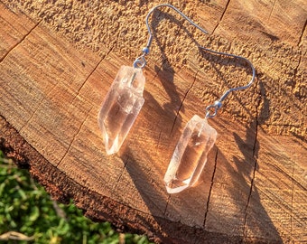 May include: A pair of silver earrings with clear quartz crystal points hanging from them. The earrings are on a wooden surface.