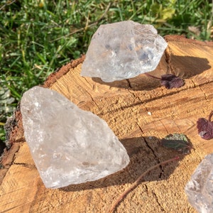 May include: Three clear quartz crystals of varying sizes and shapes on a wooden surface. The crystals are translucent and have a natural, rough texture.