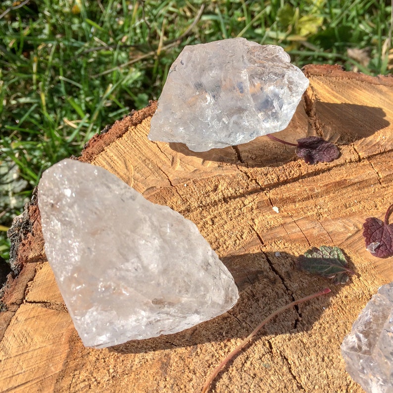 May include: Three clear quartz crystals of varying sizes and shapes on a wooden surface. The crystals are translucent and have a natural, rough texture.