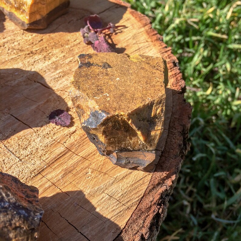 May include: A large, rough, yellow and black gemstone with a faceted surface. The gemstone is sitting on a wooden surface.