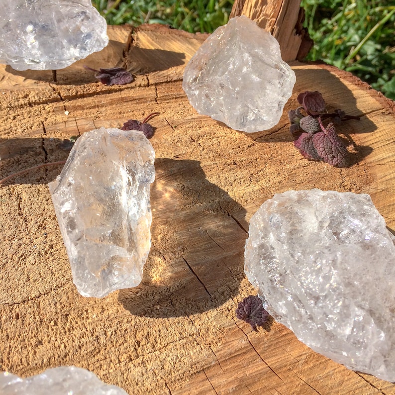 May include: Five clear quartz crystals of various sizes and shapes are arranged on a wooden surface. The crystals are translucent and have a natural, rough texture.