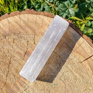 Op de afbeelding: Een witte selenietkristalstaf die op een houten oppervlak ligt. De kristal is glad en heeft een natuurlijke, gestreepte textuur.