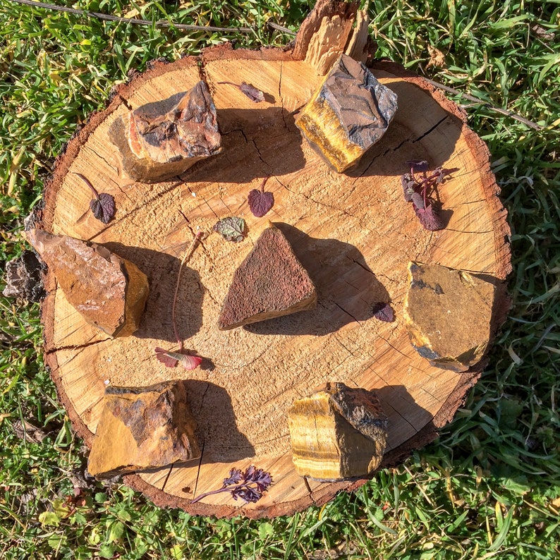 May include: A collection of six polished tiger's eye and red jasper stones on a wooden surface. The stones are arranged in a circle, with the tiger's eye stones on the outside and the red jasper stones in the center.