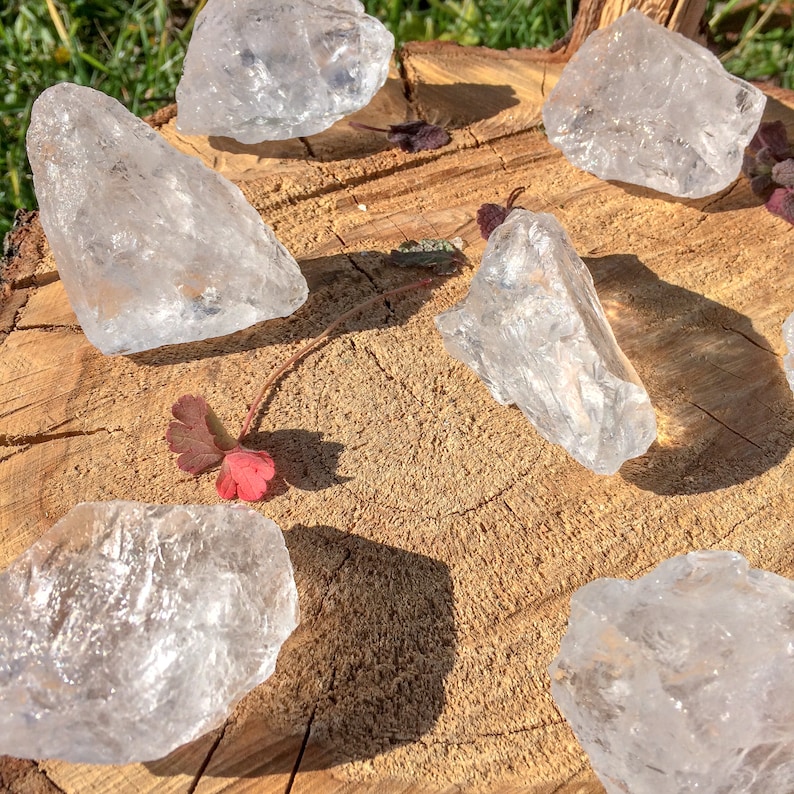 May include: A collection of six clear quartz crystals of various sizes and shapes, arranged on a wooden surface. The crystals are translucent and have a natural, rough texture.