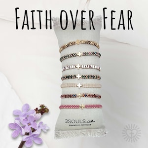 May include: A stack of eight colorful beaded bracelets with a gold cross charm on each. The bracelets are displayed on a white fabric background with the text "FAITH OVER FEAR" at the top and "3SOULS.com" at the bottom.