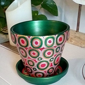 May include: A green ceramic planter with a red, white, and gold geometric pattern. The planter has a matching saucer.