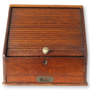 May include: A vintage wooden desk organizer with a roll-top cover. The desk organizer has a brass knob and a keyhole. The wood has a warm, reddish-brown tone, and the piece appears to be well-preserved.