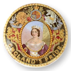 May include: A round, decorative plate featuring a portrait of a woman in a crown, surrounded by ornate gold and red detailing. The plate includes the text "ENGLAND'S PRIDE" and images of a lion, a unicorn, and a coat of arms.