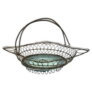 May include: An antique wire basket with a handle and a decorative glass insert. The basket is made of dark metal wire and features a handle and a decorative glass insert with a blue and white pattern.