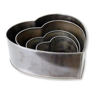 May include: Set of four nested heart-shaped cookie cutters. The cutters are made of a dull, silver-colored metal. The largest cutter is the outermost, with three smaller cutters nested inside, each a slightly smaller heart shape.