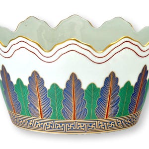 May include: A white porcelain bowl with a scalloped rim featuring a gold and red line border. The exterior displays a repeating pattern of green and blue stylized leaves with orange veins, finished with a blue and gold geometric Greek key band.