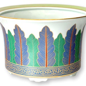 May include: A white ceramic planter featuring a repeating pattern of alternating green and blue fern-like leaves with gold outlines. The base is decorated with a blue and gold Greek key border, and the rim is finished with a thin gold band.