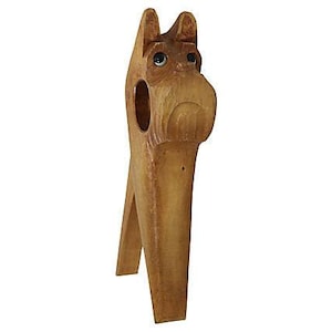 May include: A wooden dog-shaped wine bottle holder. The holder is carved from light brown wood and features a dog's head with black eyes and a snout. The bottle holder has a slot to hold a wine bottle.