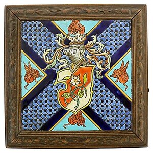 May include: Square framed tile with a detailed heraldic design. The central shield features an orange and white floral emblem, surrounded by blue scale-like patterns and accented with orange winged creatures. The frame is a dark, carved wood.