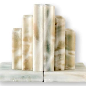 May include: A set of marble bookends. The bookends are rectangular with a light green base and vertical columns in shades of white, beige, and green. The columns are of varying heights and have rounded tops.