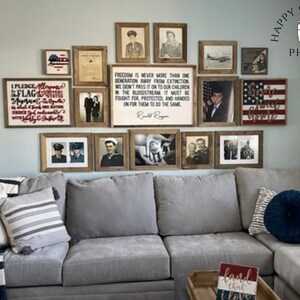 May include: A gray sectional sofa with pillows and a throw blanket. The wall behind the sofa is decorated with framed pictures and signs with patriotic themes, including the American flag, a quote about freedom, and a sign that says "Home Sweet Home".