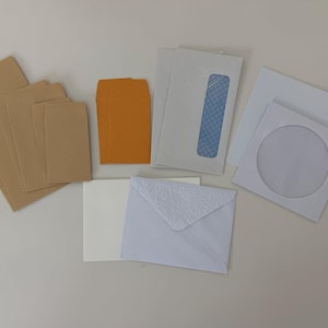May include: A collection of various envelopes including several tan rectangular envelopes, two small mustard yellow envelopes, white business envelopes with blue security patterns, a white square envelope with a circular window, and a white envelope with a floral embossed flap.