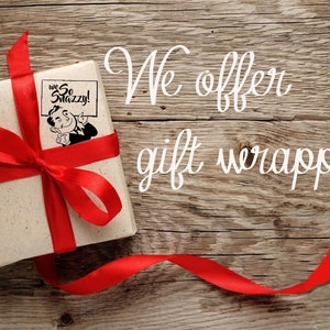 May include: A brown gift box wrapped in red ribbon with a bow on top. The box has a sticker on it that says "We So Snazzy!" The box is sitting on a wooden surface. The text "We offer gift wrapping!" is written in white on the wooden surface.