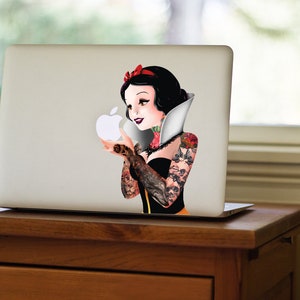 May include: A white laptop with a sticker of Snow White with tattoos holding a white apple. The sticker is on the back of the laptop.
