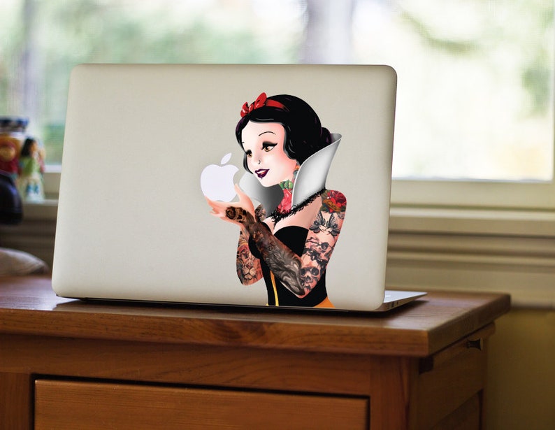 May include: A white laptop with a sticker of Snow White with tattoos holding a white apple. The sticker is on the back of the laptop.