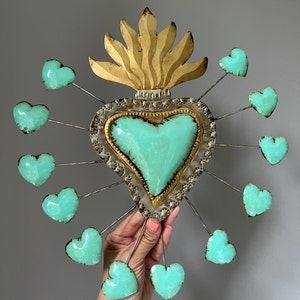 May include: A metal heart with a turquoise center and gold accents surrounded by 12 smaller turquoise hearts. The larger heart has a flame design at the top.