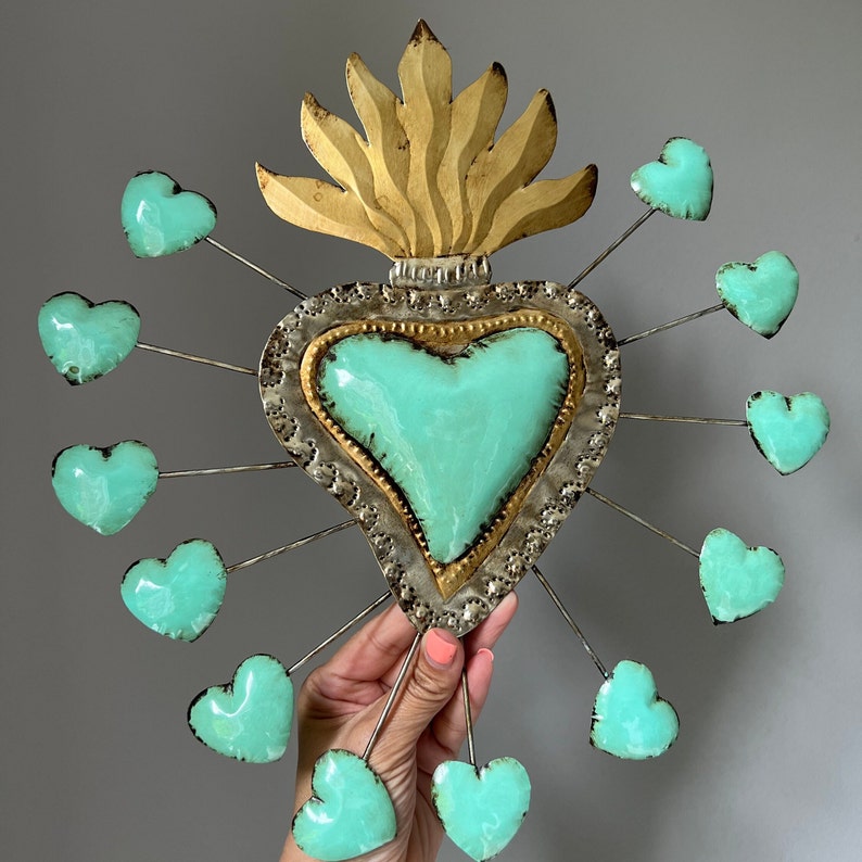 May include: A metal heart with a turquoise center and gold accents surrounded by 12 smaller turquoise hearts. The larger heart has a flame design at the top.