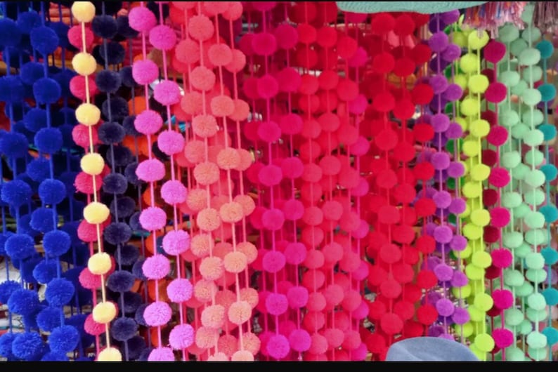May include: A selection of colourful pom-pom trim, with strands of blue, yellow, pink, red, purple, green, and lime green pom-poms.