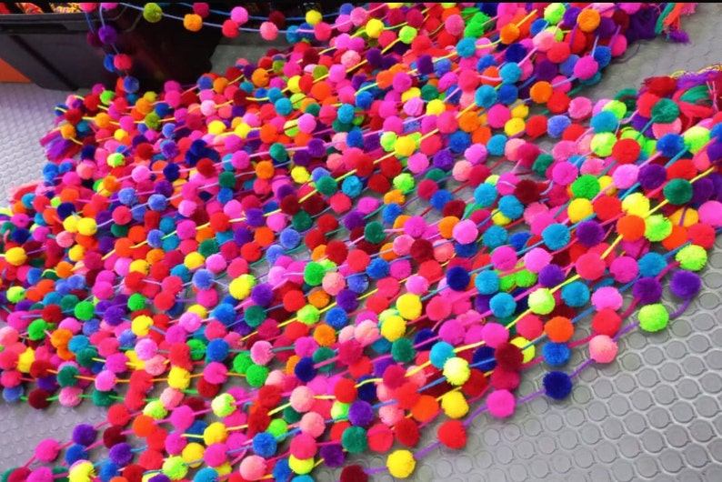 May include: A colourful garland of pom-poms in various shades of pink, purple, blue, green, yellow, orange, and red. The pom-poms are strung together on a thin string.