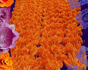 Puede incluir: Una colección de guirnaldas de flores de color naranja brillante estilo caléndula hechas de fibras sintéticas. Las hebras presentan numerosas flores esféricas pequeñas y densamente agrupadas en filas verticales, terminadas en borlas.