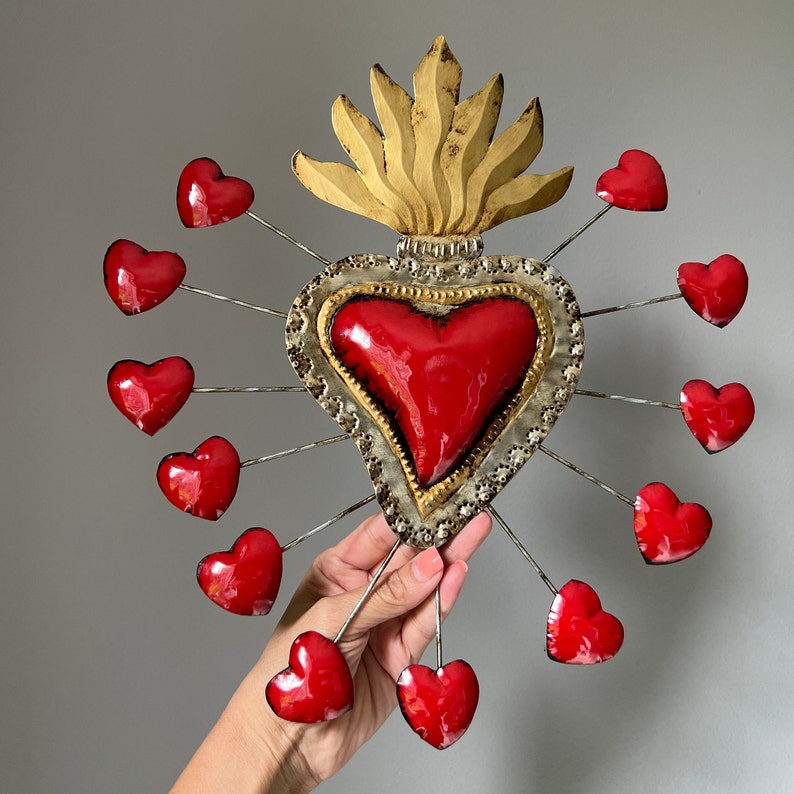 May include: A large, red, metal heart with a gold flame design and 12 smaller red hearts surrounding it. The hearts are attached to the larger heart with metal rods.