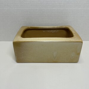 May include: A rectangular ceramic planter with a smooth, glossy finish in a light beige or tan color. The vessel features a wide, open top with rounded corners and a solid, flat base, presenting a clean, simple design for holding small items.