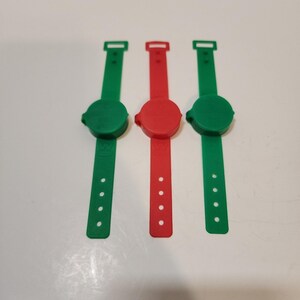 May include: Three silicone wristbands, two green and one red, each featuring a circular center disc and a strap with four adjustment holes. The letter W is embossed on the lower portion of each strap, providing a uniform design across all three items.