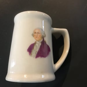 Könnte beinhalten: Weiße Keramiktasse mit einem Porträt von George Washington in einem violetten Mantel und einem weißen Hemd.