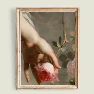 Puede incluir: Una mano se extiende para sostener una rosa rosa con hojas verdes y espinas. El fondo es de un gris apagado.