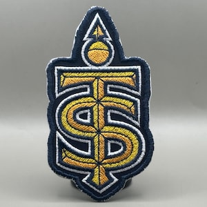May include: Embroidered patch featuring a stylized design in navy blue, gold, and white. The design includes the letters "TS" intertwined with an anchor symbol. The patch has a navy blue border and is likely for apparel or accessories.