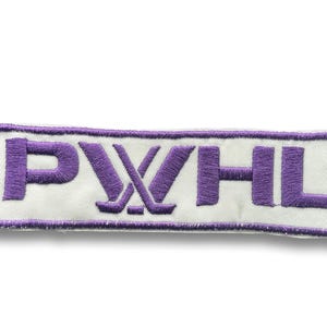 May include: Embroidered patch with the letters PWHL in purple, with crossed hockey sticks in the center. The text is on a white background, framed by a purple border. The patch is rectangular.