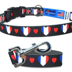 May include: A black dog collar and leash with a repeating pattern of red hearts and white hearts with the French flag colors. The collar has a black plastic buckle and a silver D-ring. The leash has a silver clip. The collar and leash are labeled "FlagCollars.com" and "Made in the USA".