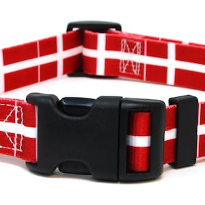 May include: Red and white dog collar with a black plastic buckle and a silver D-ring. The collar features a repeating pattern of the Danish flag.