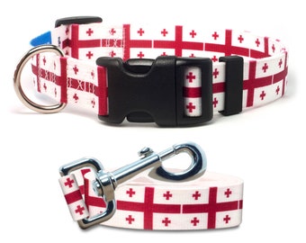 May include: A white and red dog collar and leash with a repeating pattern of the Georgian flag. The collar has a black plastic buckle and a silver D-ring. The leash has a silver clip.