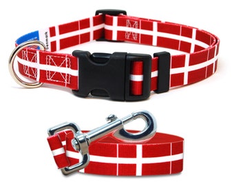 May include: Red and white dog collar and leash set. The collar and leash feature a repeating pattern of a white cross on a red background. The collar has a black plastic buckle and a metal D-ring. The leash has a metal clasp.