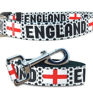 May include: Black and white dog collar and leash with a soccer ball pattern and the word "ENGLAND" repeated. The collar has a silver D-ring and a black plastic buckle. The leash has a silver clip. Both feature a red and white English flag.